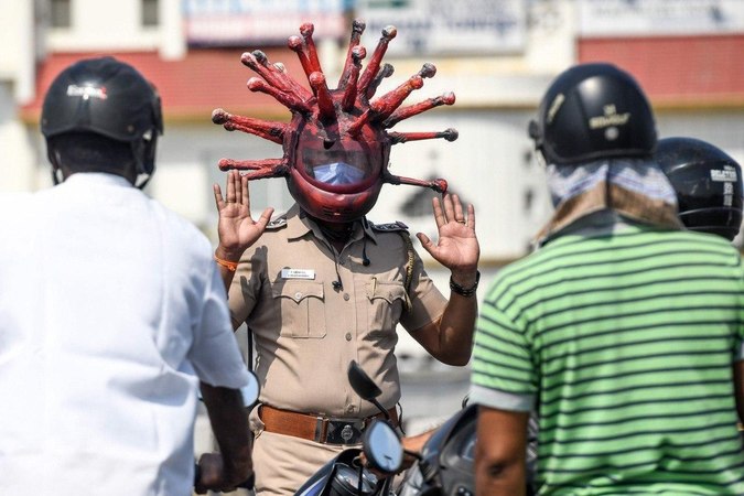 Полицейский Раджеш Бабу из индийского города Ченнаи во время патрулирования надевает шлем, изображающий модель коронавируса.